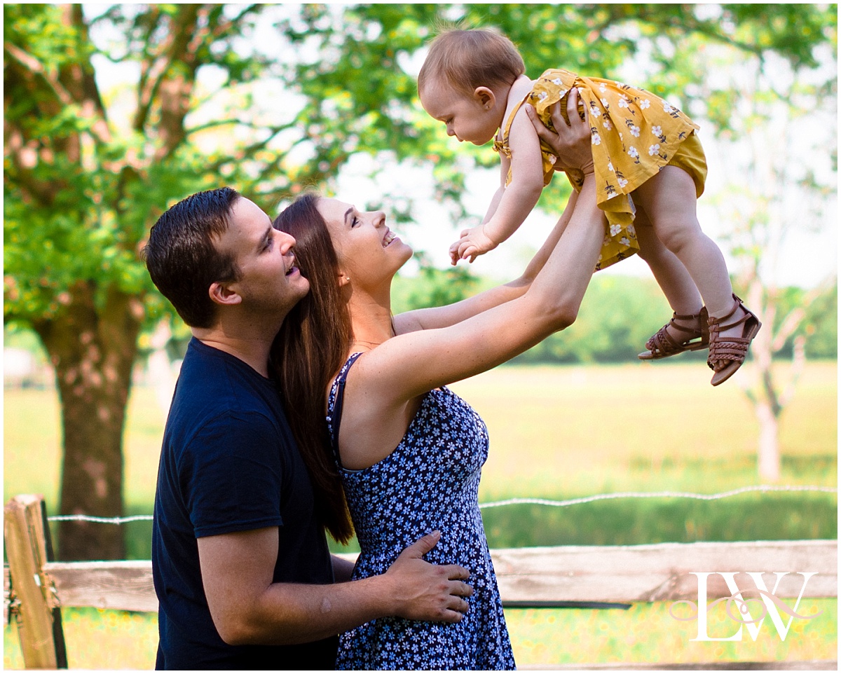 Currituck Family photo session beautiful young couple hold their baby up in the air on a farm.