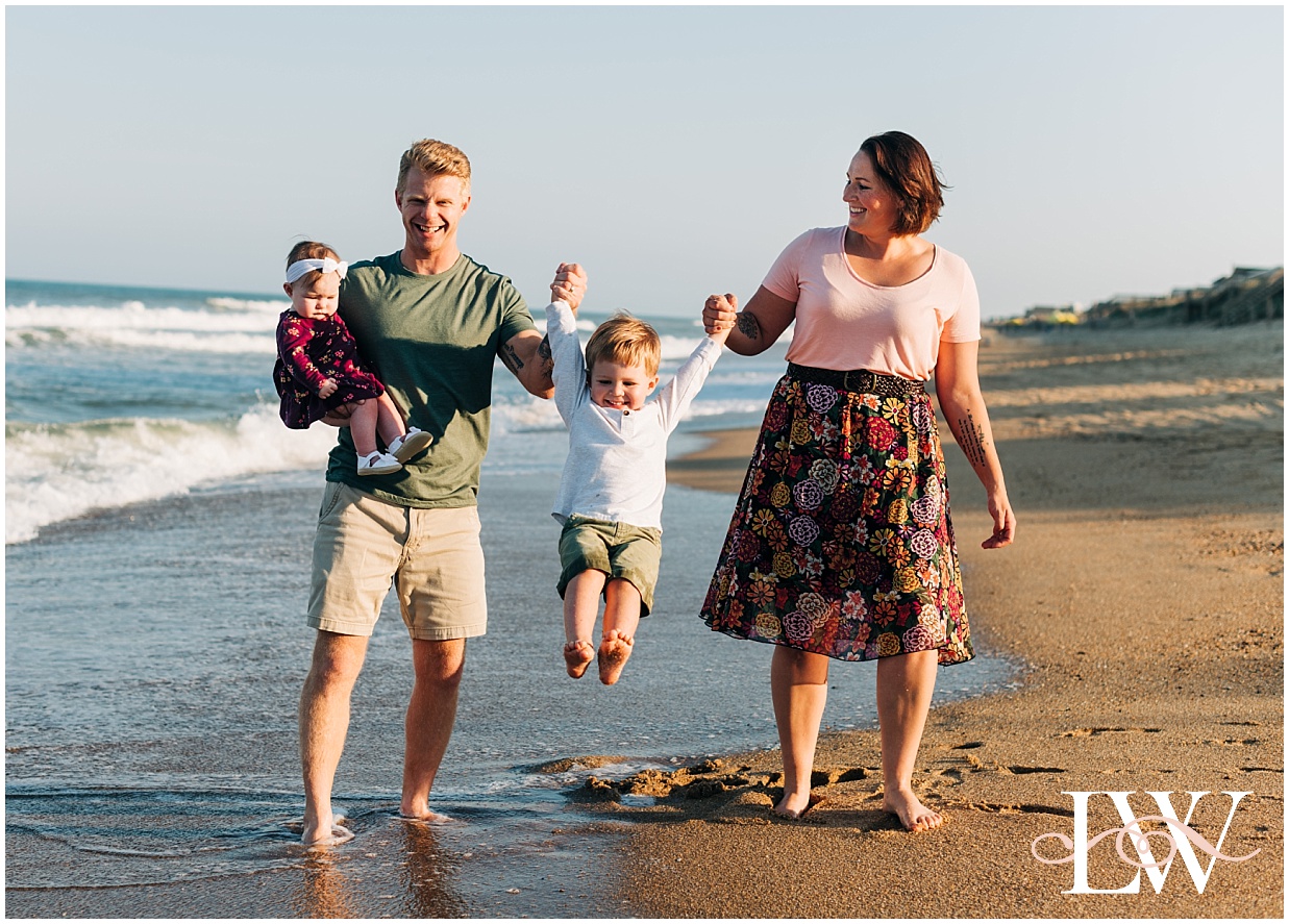Mom and dad swinging a little boy by the waterside holding a baby in Duck, NC Beach Family Session on the Outer Banks by Laura Walter Photography
