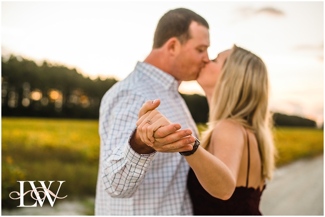 Engaged couple kissing and dancing  with focus on the ring by a yellow field in Currituck, taken by Laura Walter Photography.