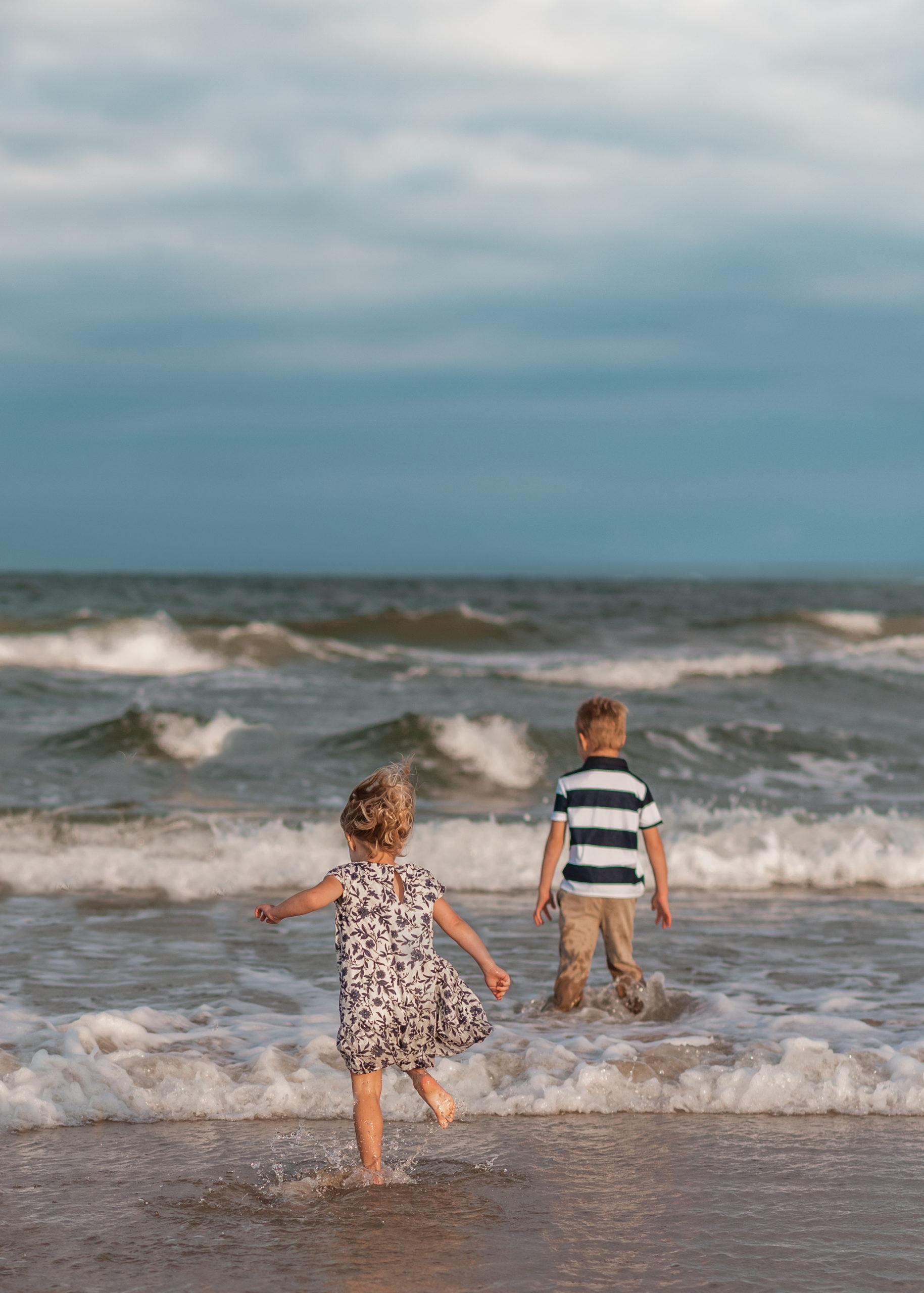 brother and sister running into the ocean from behind by laura walter photography