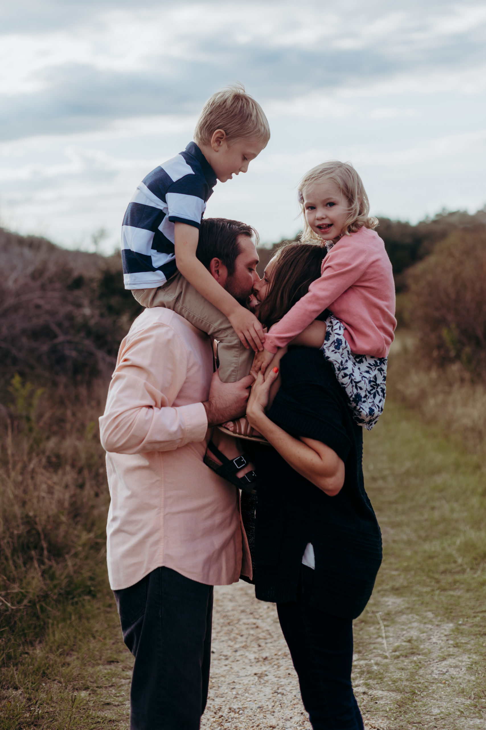 mom and dad kiss with brother and sister sitting on their shoulders, Outer Banks fun and natural family photographer Laura Walter