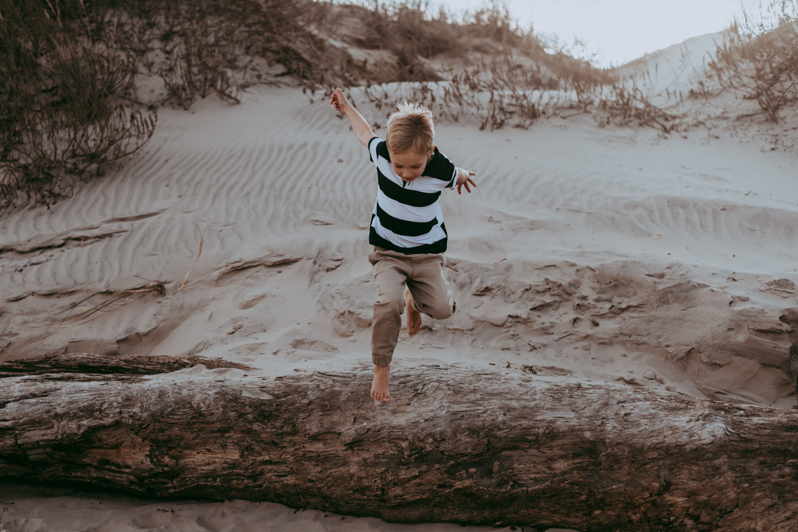 boy jumping off of a big tree trunk on the beach