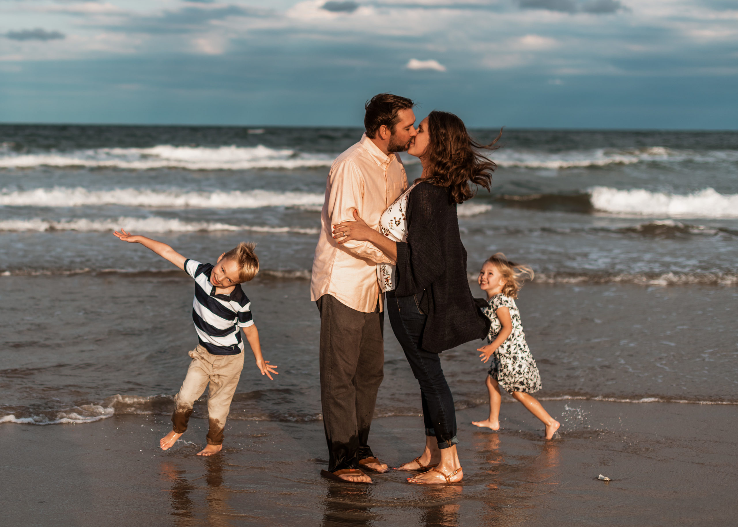 mom and dad kiss y the ocean while kids run around them 