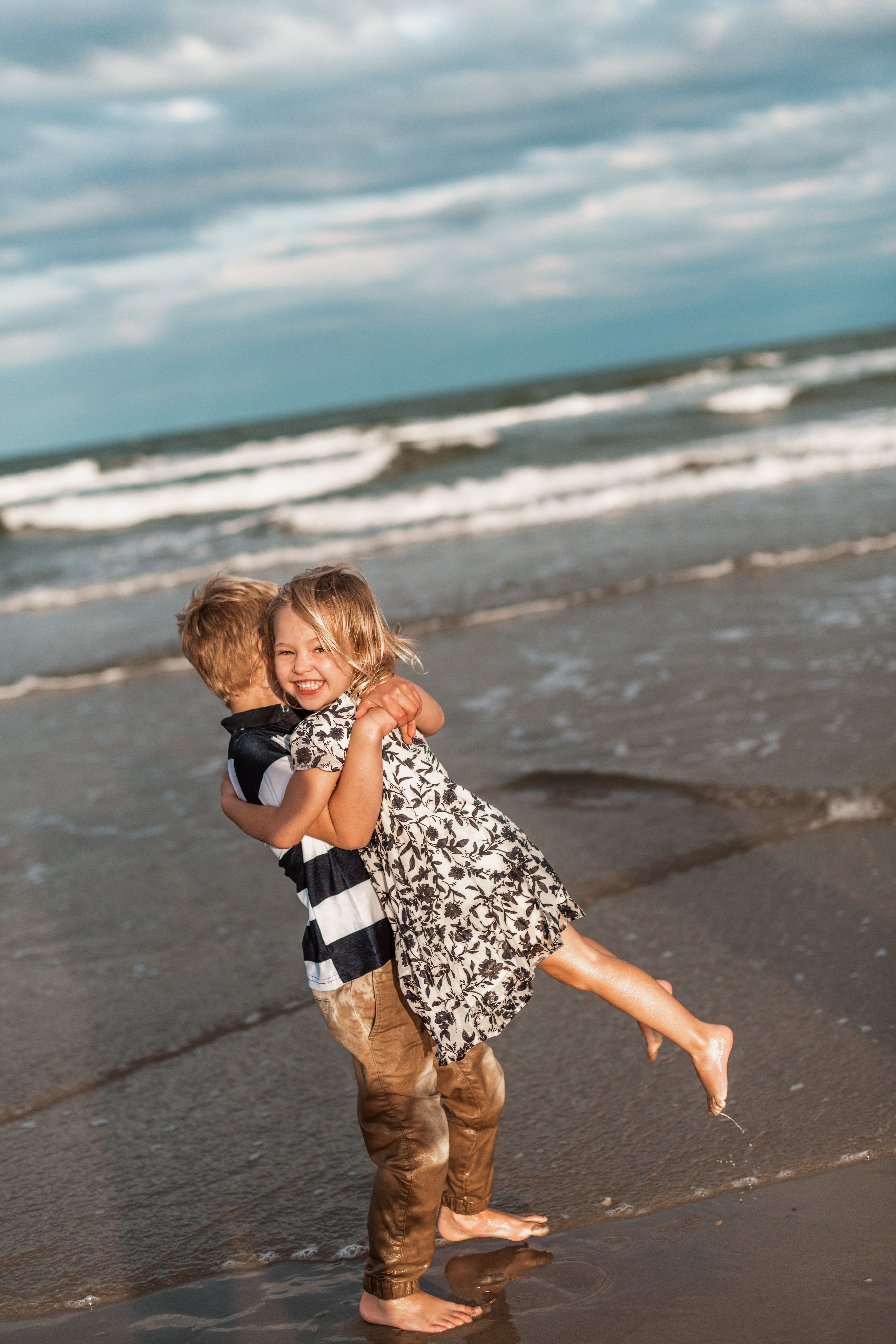 big brother swinging sister around in the ocean Outer Banks fun and natural family photographer Laura Walter