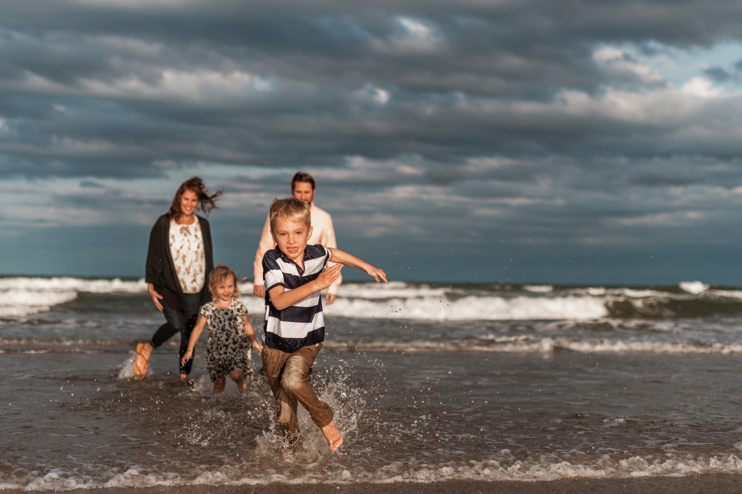 family standing in the ocean little boy running towards the camera