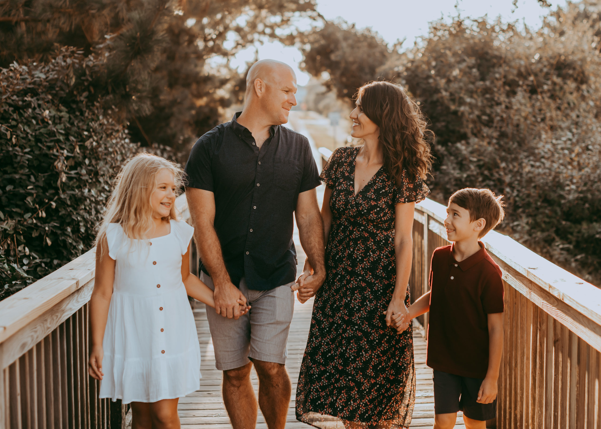 family of four walking on the deck to the beach, smiling and holding hands Family Photo Session by Laura Walter Photography