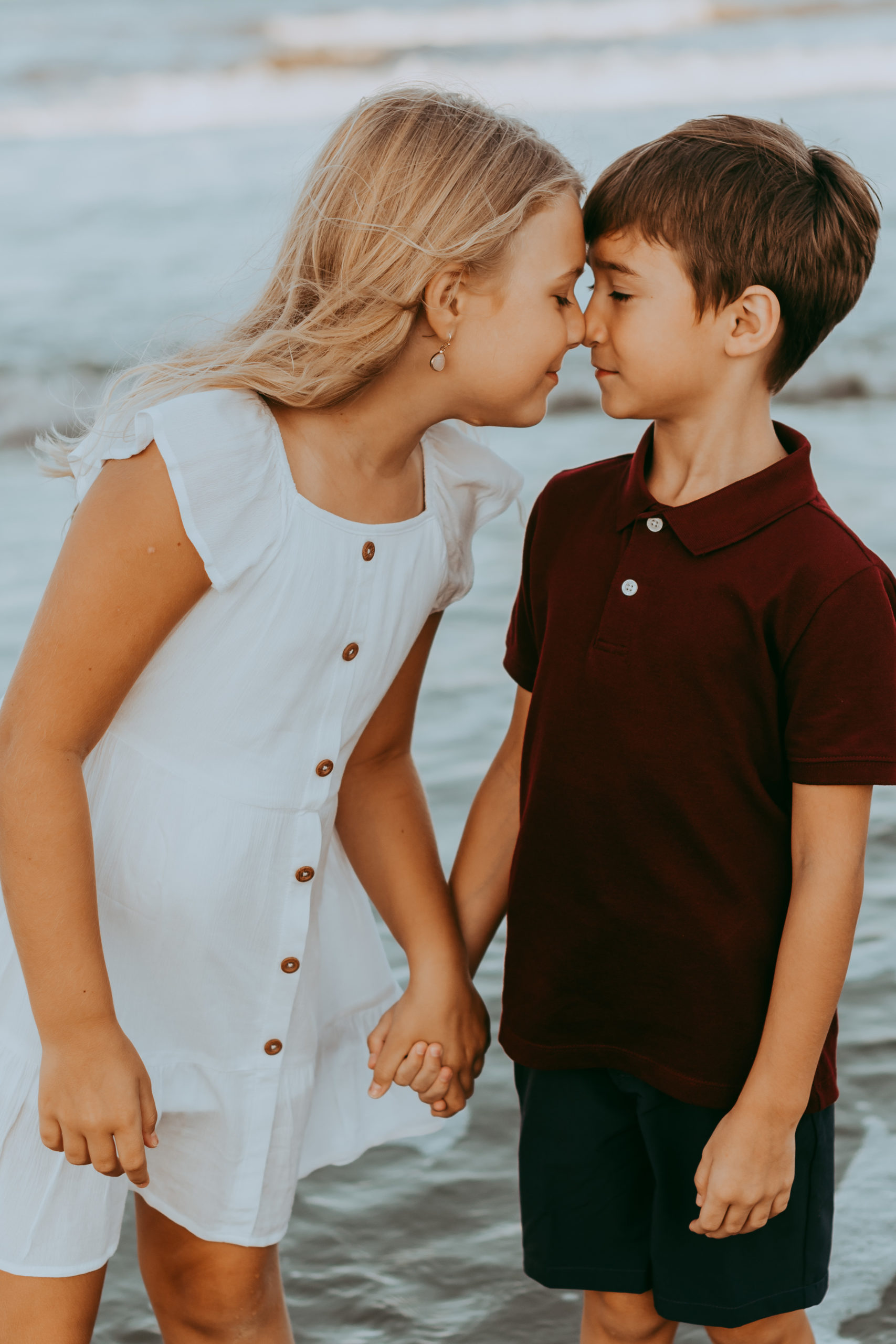 big sister trying to give brother a kiss in the ocean Family Photo Sessions in Corolla by Laura Walter Photography