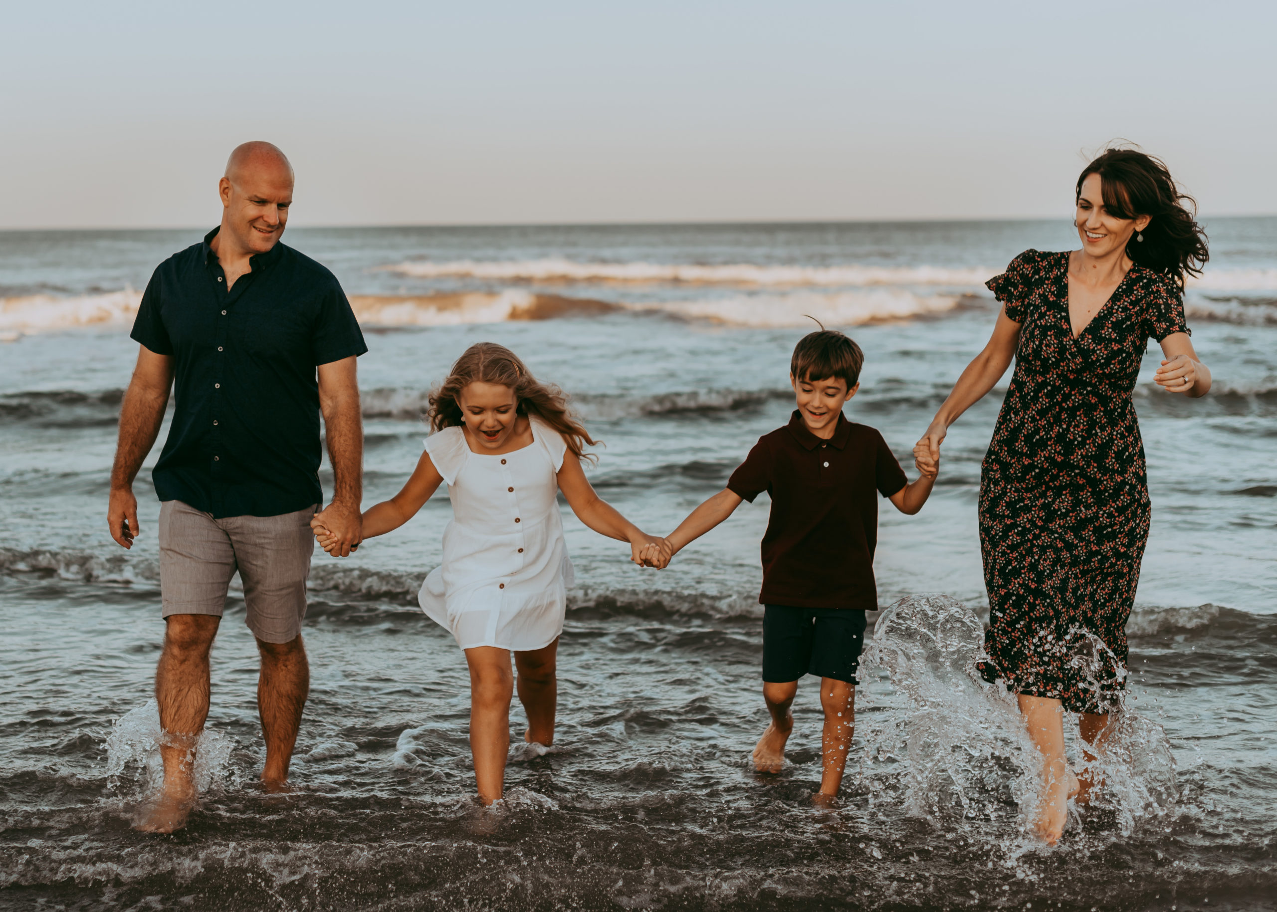 Family Photo Sessions in Corolla by Laura Walter Photography family running out of the ocean together holding hands
